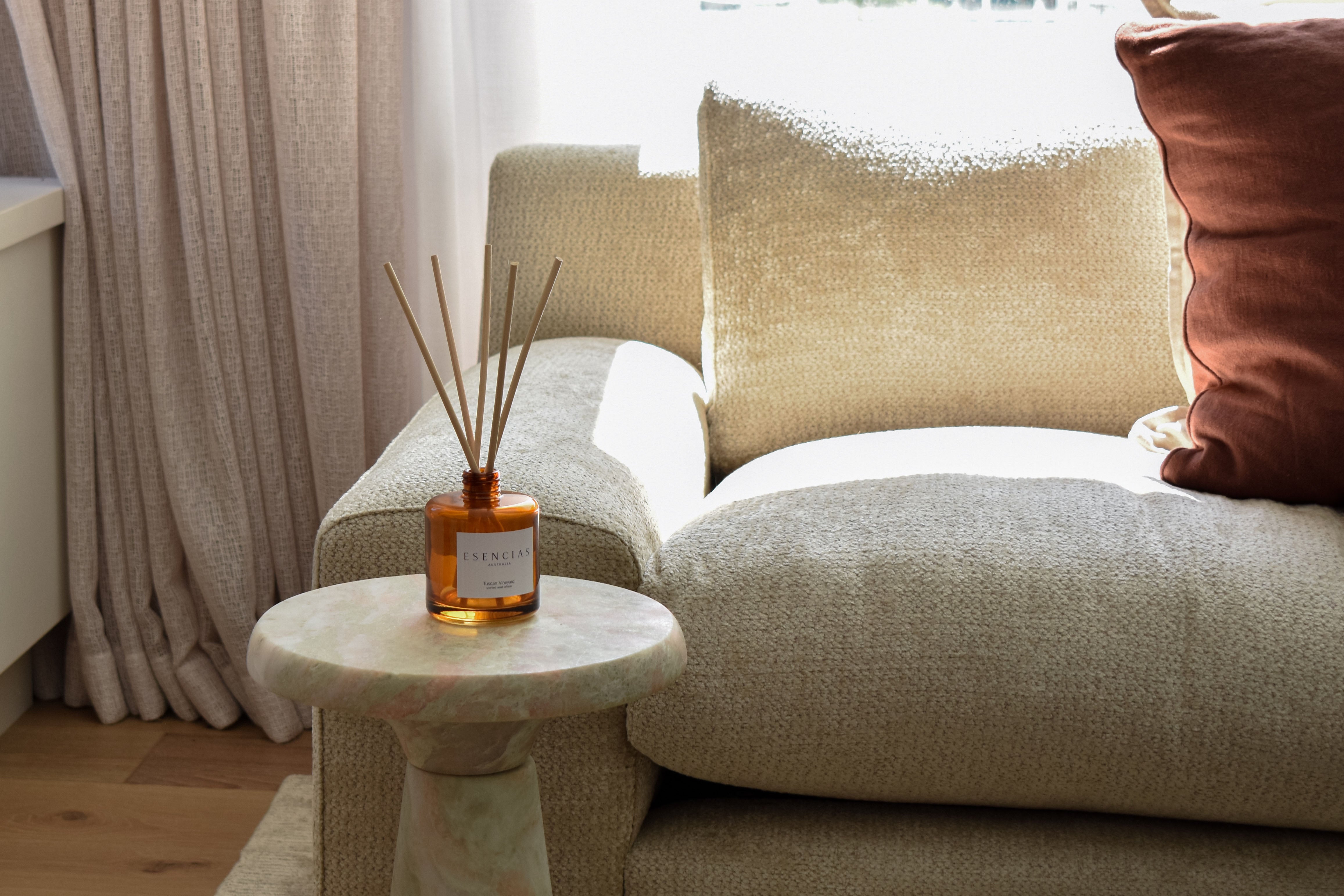 Tuscan Vineyard reed diffuser in signature amber jar shown in a wider living room lifestyle shot, capturing a warm, inviting space with rustic elegance.