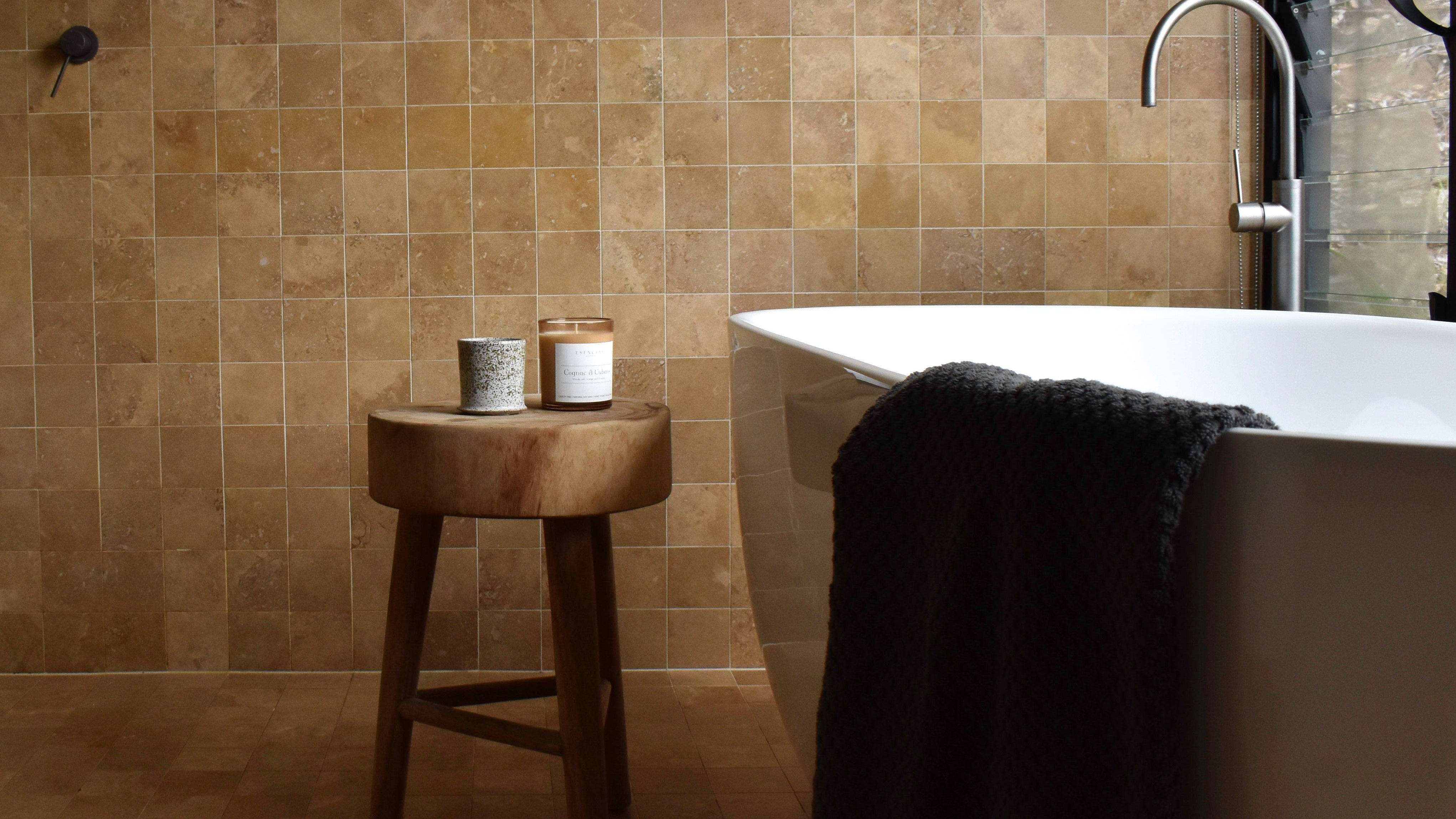 Modern bathroom with a freestanding bathtub, wooden stool, and tiled walls.