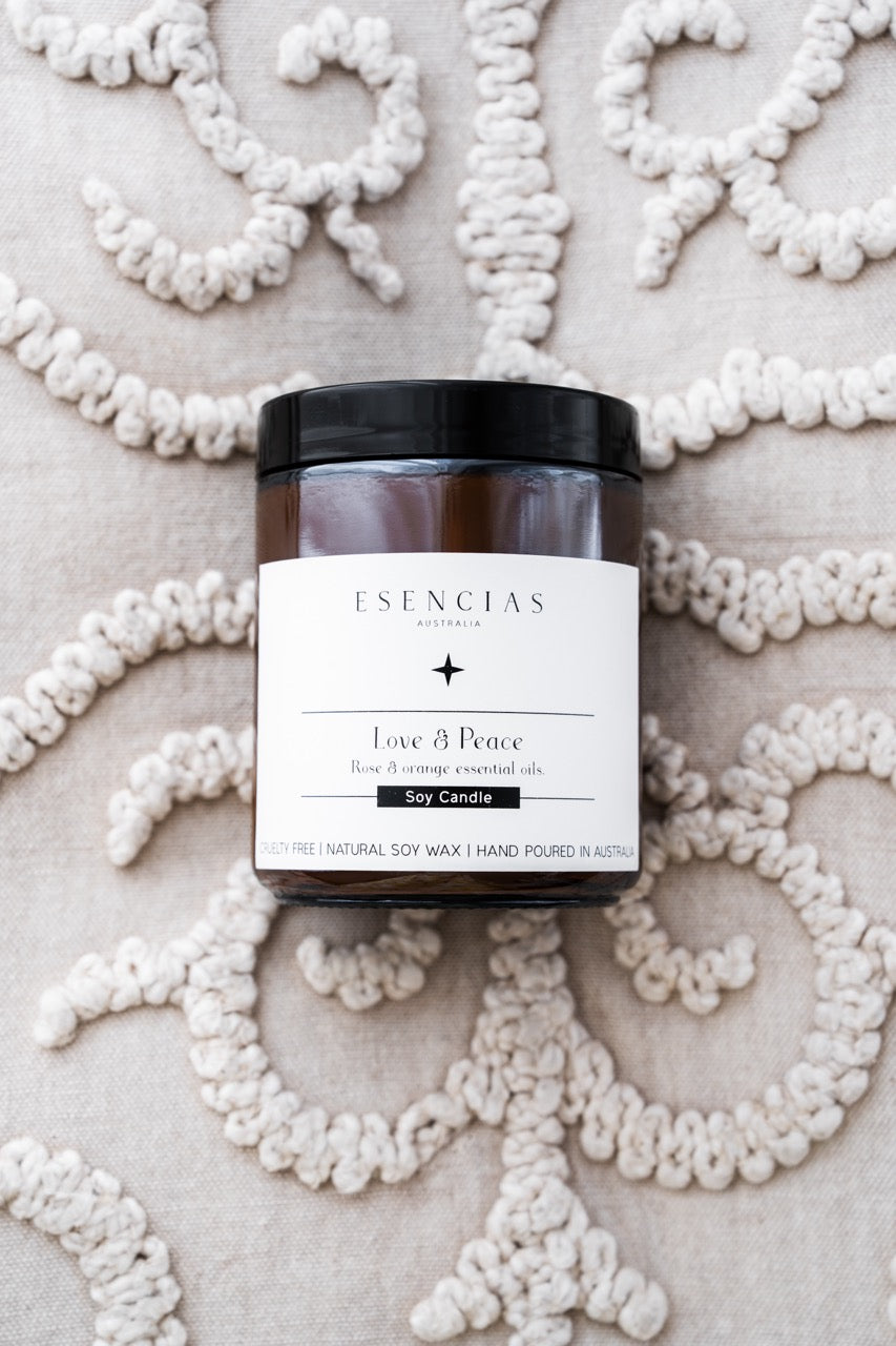 Love and Peace soy candle jar labeled 'Esencias' on a decorative white background