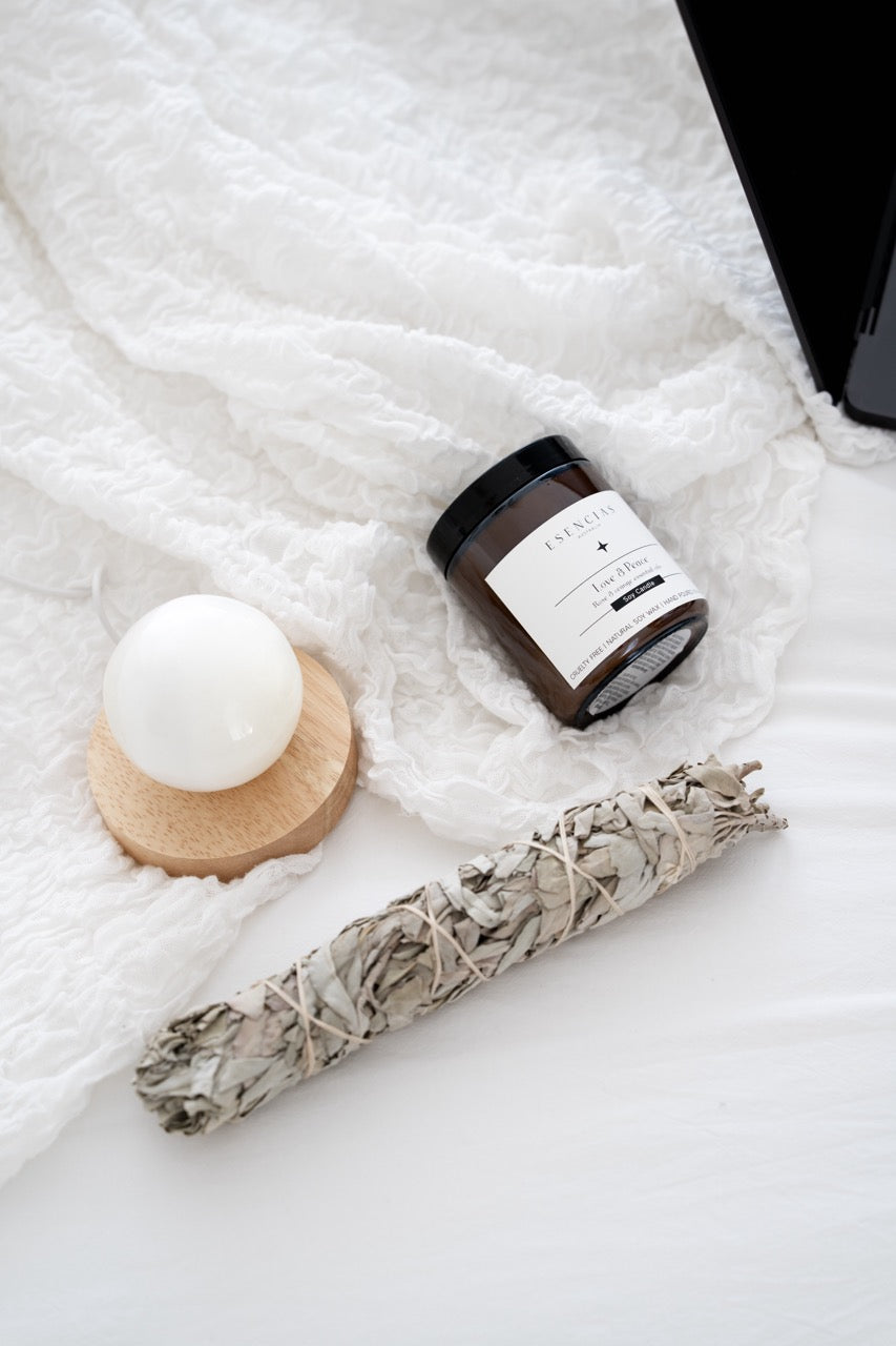 Love & Peace soy candle, sage bundle, and selenite sphere on a textured white surface
