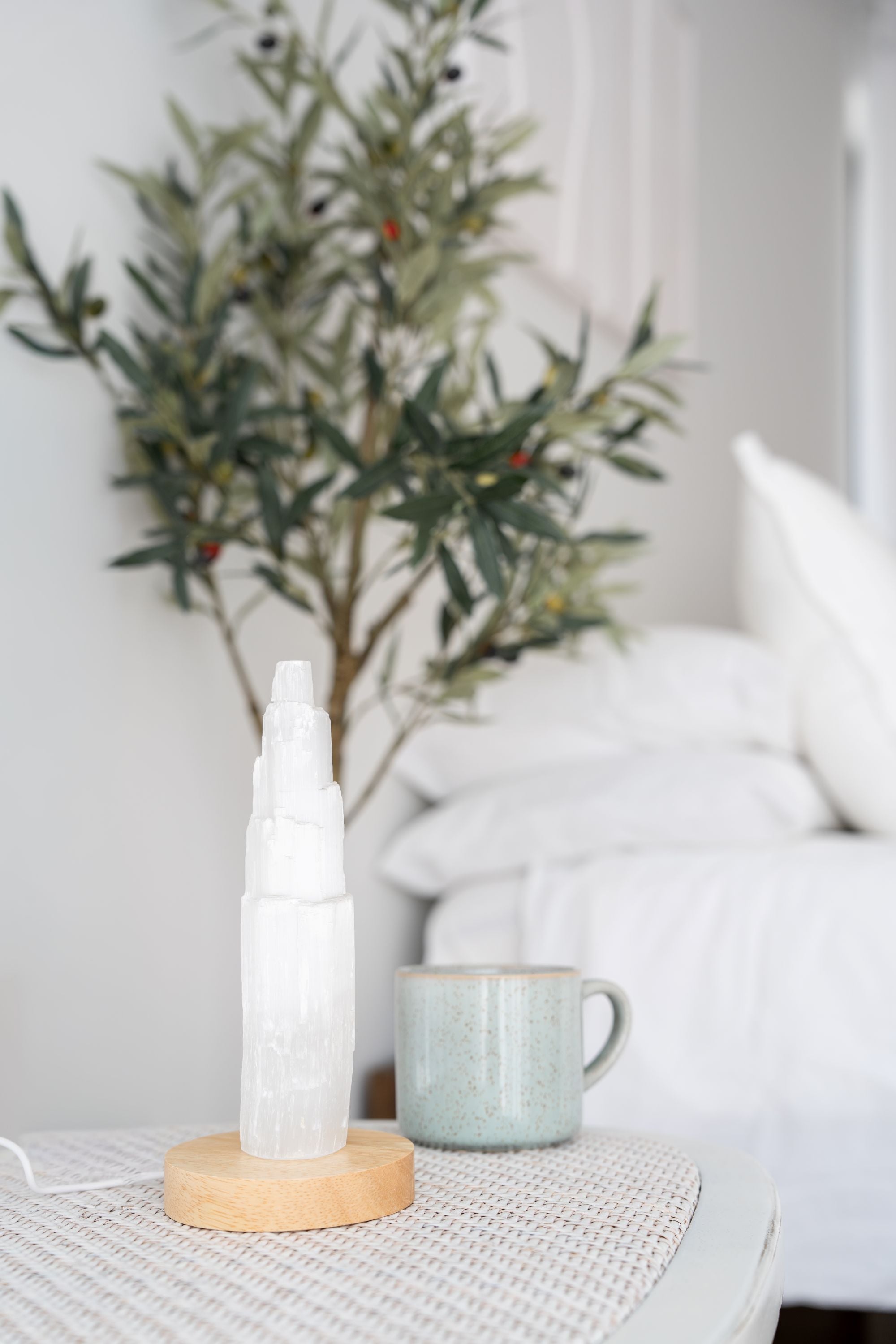 Selenite crystal on a wooden LED light base with a plant and mug in the background