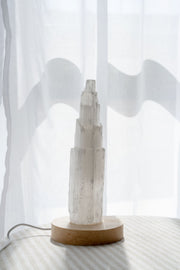 Selenite tower on wooden LED light base against a white curtain background