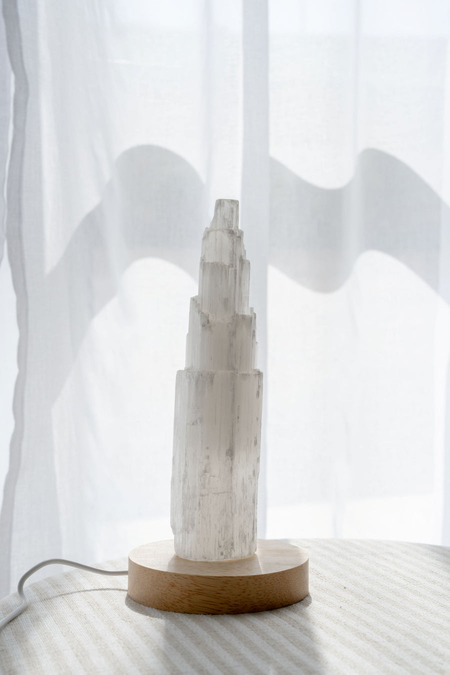 Selenite tower on wooden LED light base against a white curtain background
