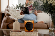 Signature Luxe Candle in Havana Sunset styled with plants and blurred background. 