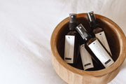 All four Esencias room sprays – Calming & Intuition, Love & Peace, Angelic Radiance and Revitalise & Cleanse – resting in a wooden bowl on soft white linen