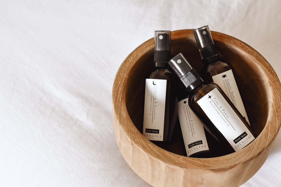 All four Esencias room sprays – Calming & Intuition, Love & Peace, Angelic Radiance and Revitalise & Cleanse – resting in a wooden bowl on soft white linen