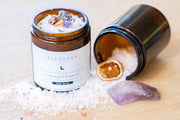 Close-up of open Esencias soak scrub jars with one spilled to show texture and contents