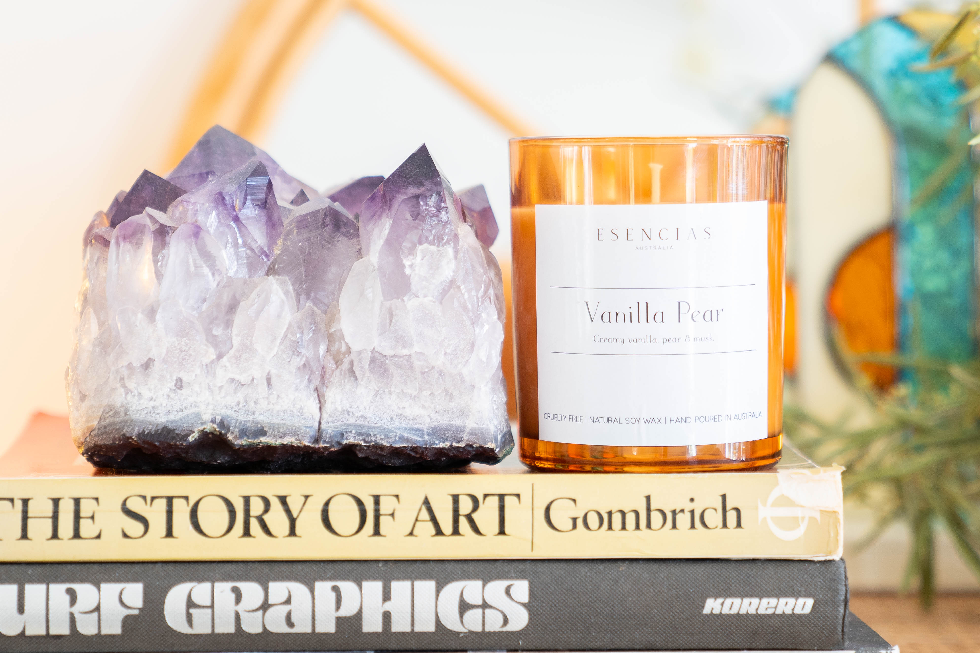 Esencias Vanilla Pear soy candle with amethyst crystal on stacked books for a calming touch
