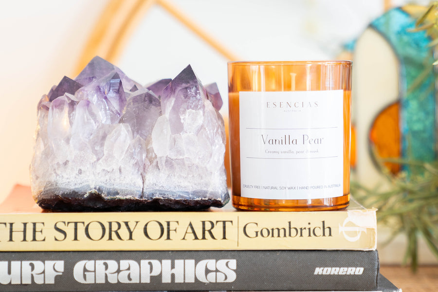 Esencias Vanilla Pear soy candle with amethyst crystal on stacked books for a calming touch
