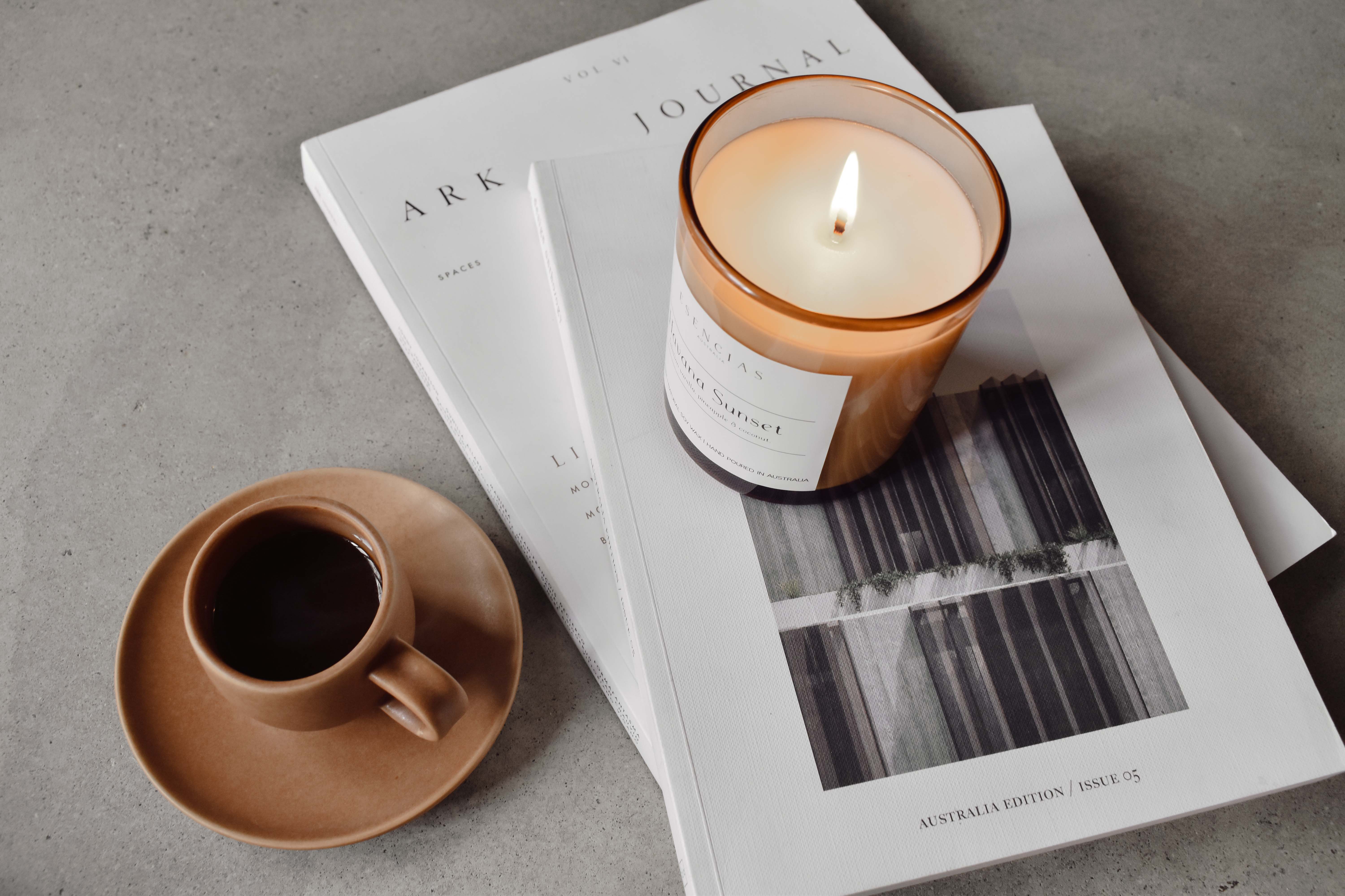Havana Sunset amber jar candle lit and styled in a cozy lifestyle setting with a cup of coffee and magazine, evoking warmth and relaxed comfort.