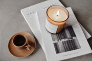 Havana Sunset amber jar candle lit and styled in a cozy lifestyle setting with a cup of coffee and magazine, evoking warmth and relaxed comfort.