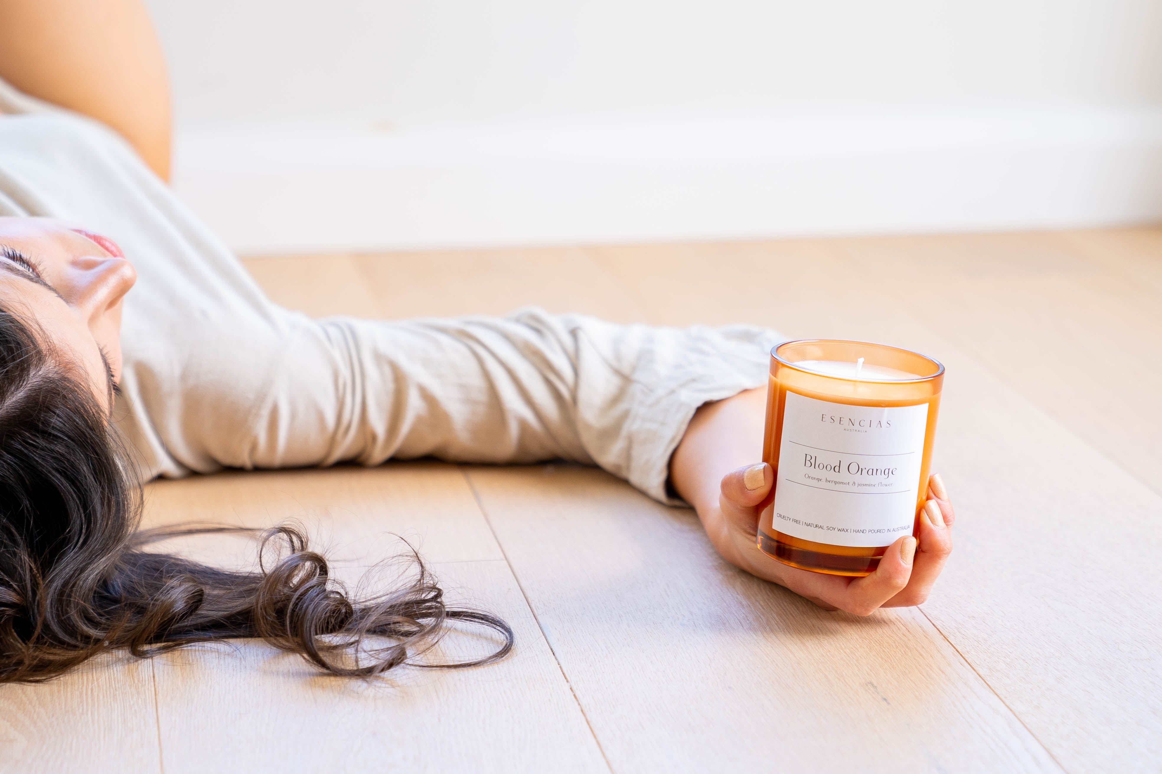 Model holding a Blood Orange soy candle in an amber jar, showcasing the product in a warm, inviting lifestyle setting.