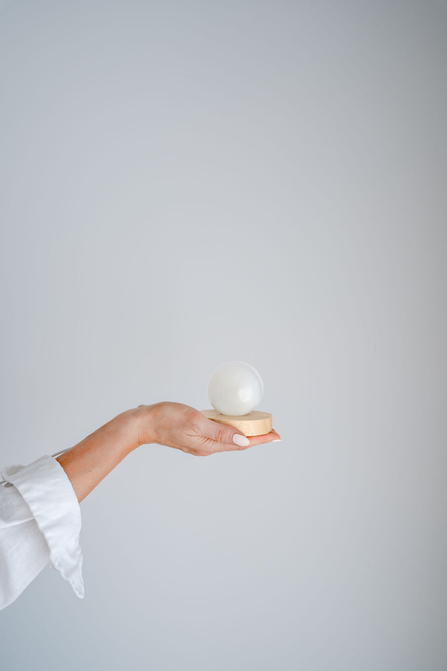 Hand holding selenite sphere with LED lamp against a plain background