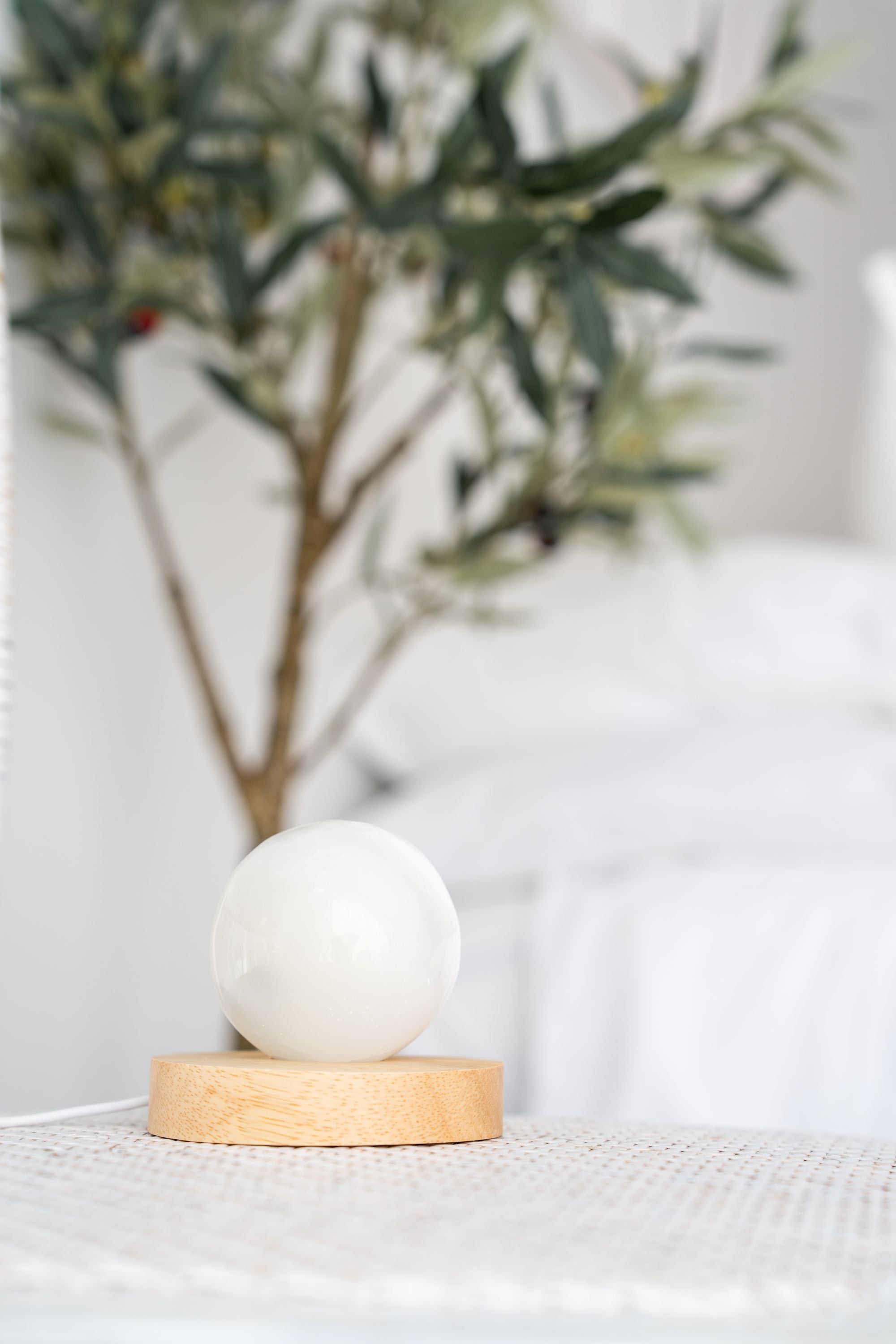 selenite sphere with LED lamp on a wooden base with a blurred plant in the background