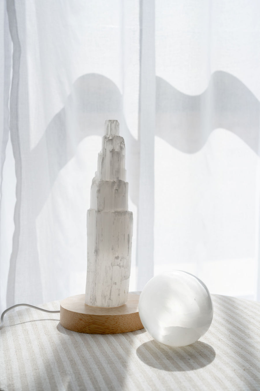 Selenite sphere and selenite tower together next to sheer curtian