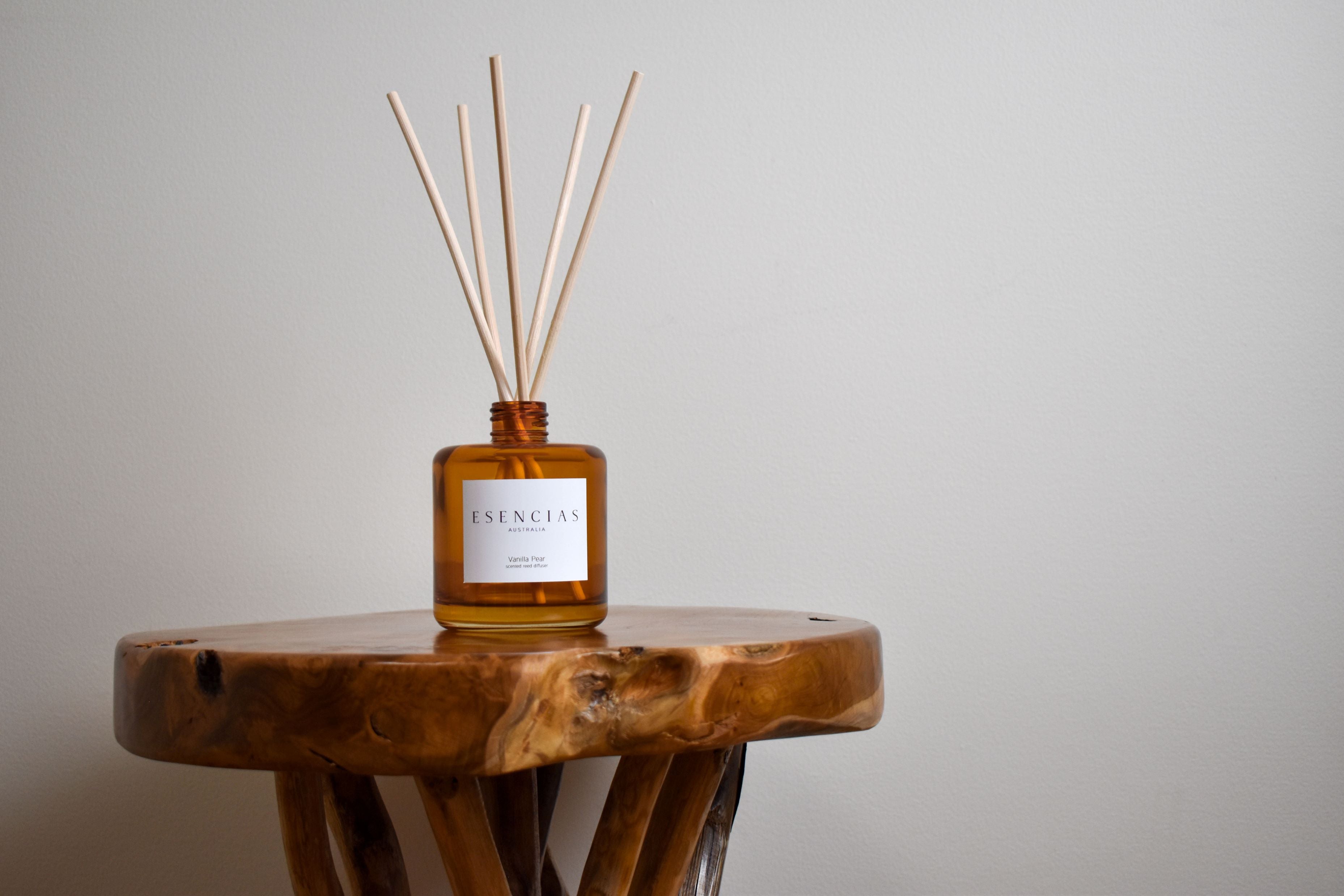 Vanilla Pear reed diffuser in amber jar styled on natural timber surface, evoking warmth and rustic elegance in a product-focused image.